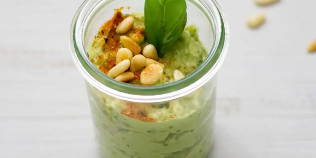 Cremiges Avocado Pesto in einem Glas, garniert mit Pinienkernen, Basilikum und Paprikapulver. Ein Genuss für jeden Tag!