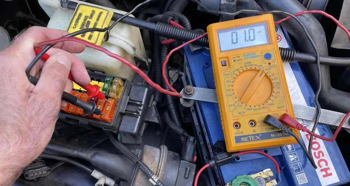 Testing for a parasitic draw with a multimeter connected to the car battery. A reading of 01.0 mV indicates a small current drain.