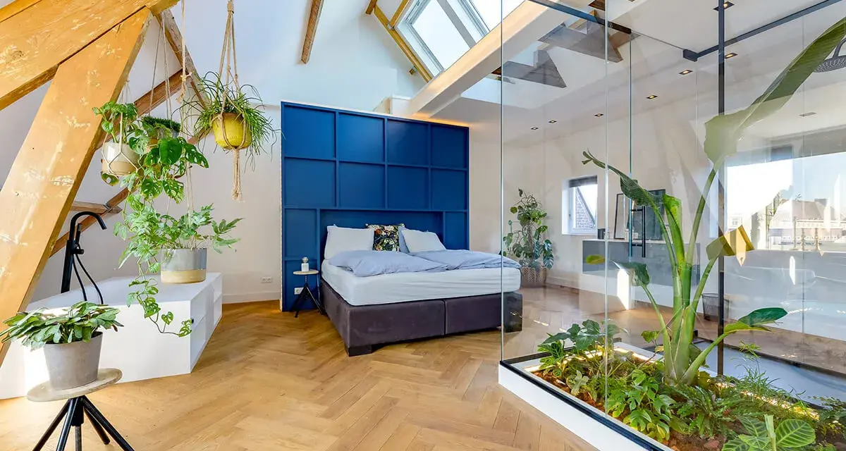 Mansarde da sogno con letto blu, piante sospese e un giardino interno in vetro. Travi a vista e lucernari creano un'atmosfera unica.