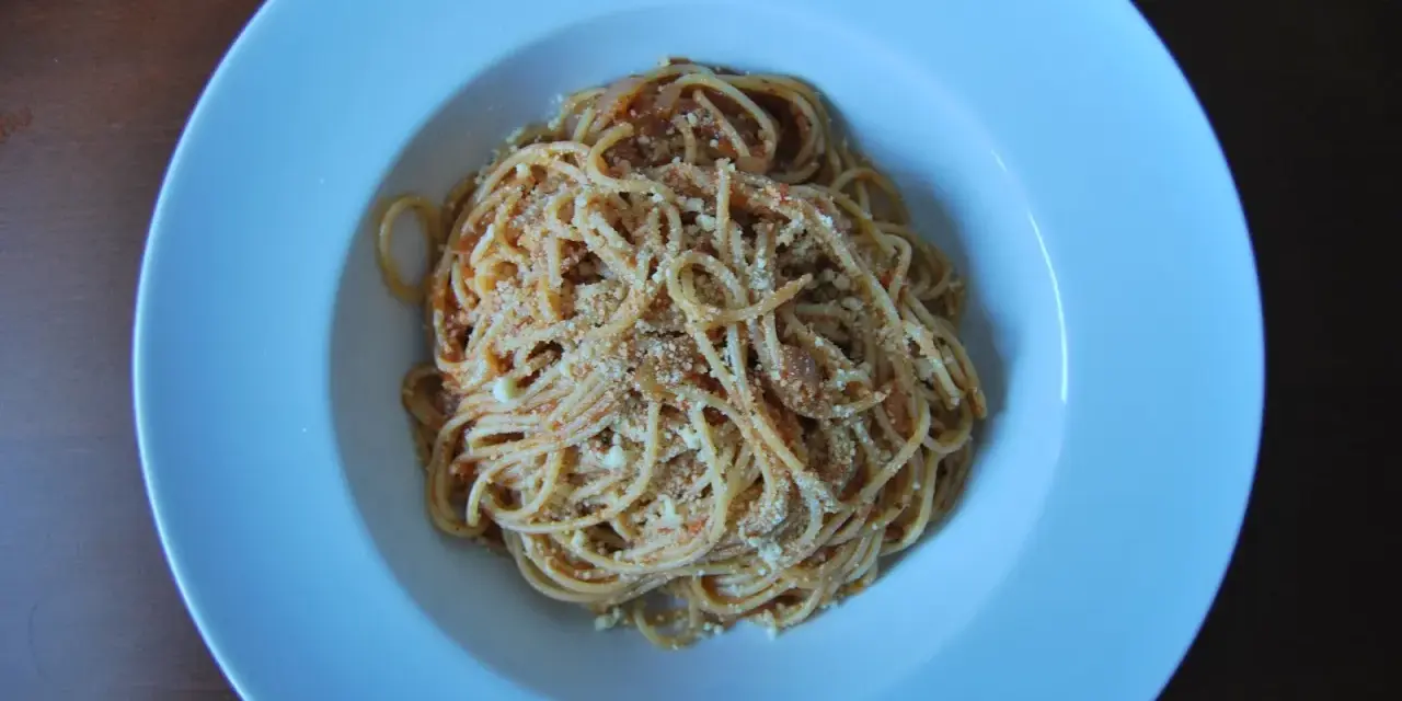 Spaghetti Napoli z sosem pomidorowym i parmezanem, podane w białej głębokiej misce.