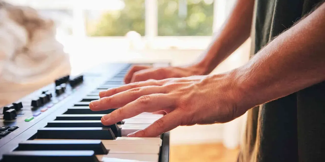 Dłonie grające na keyboardzie. To instrument muzyczny, który pozwala tworzyć melodie.