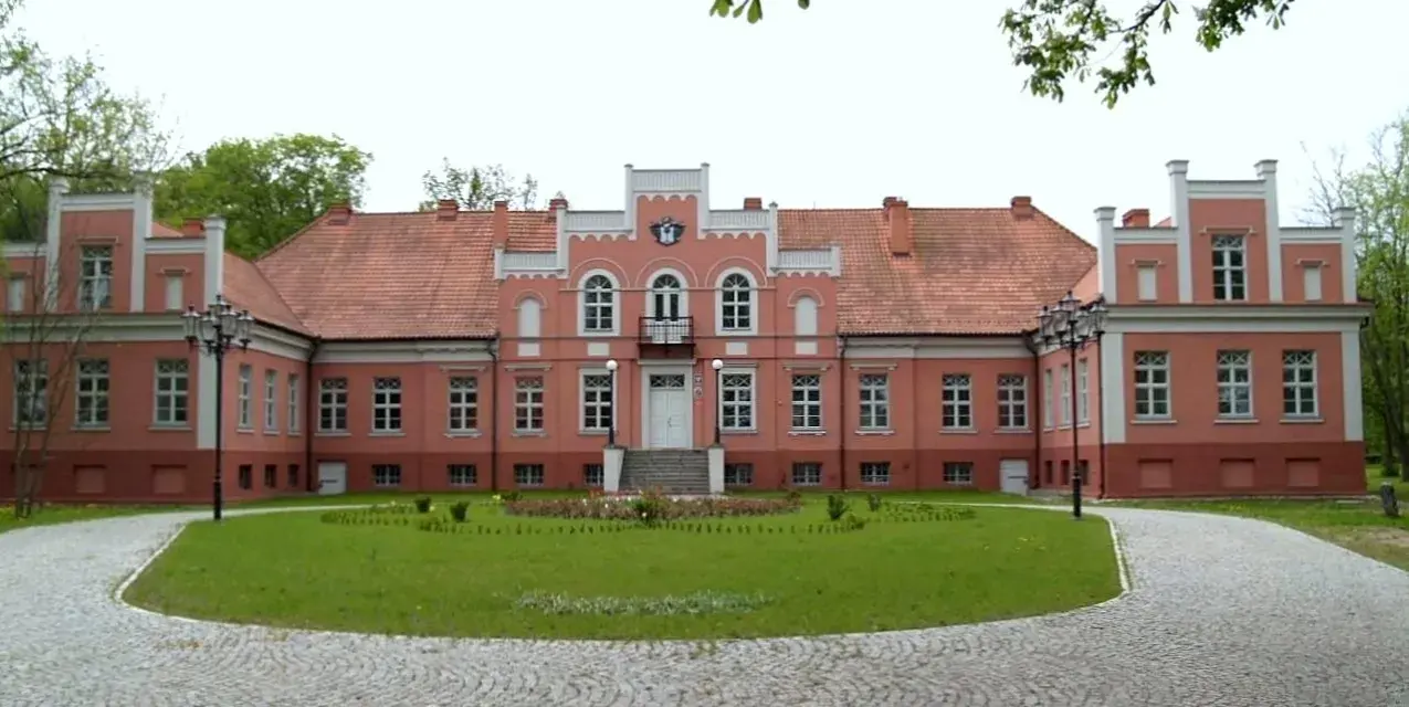 Pałac Przebendowskich w Wejherowie, różowy, z czerwonym dachem, otoczony zielenią i brukowanymi alejkami.