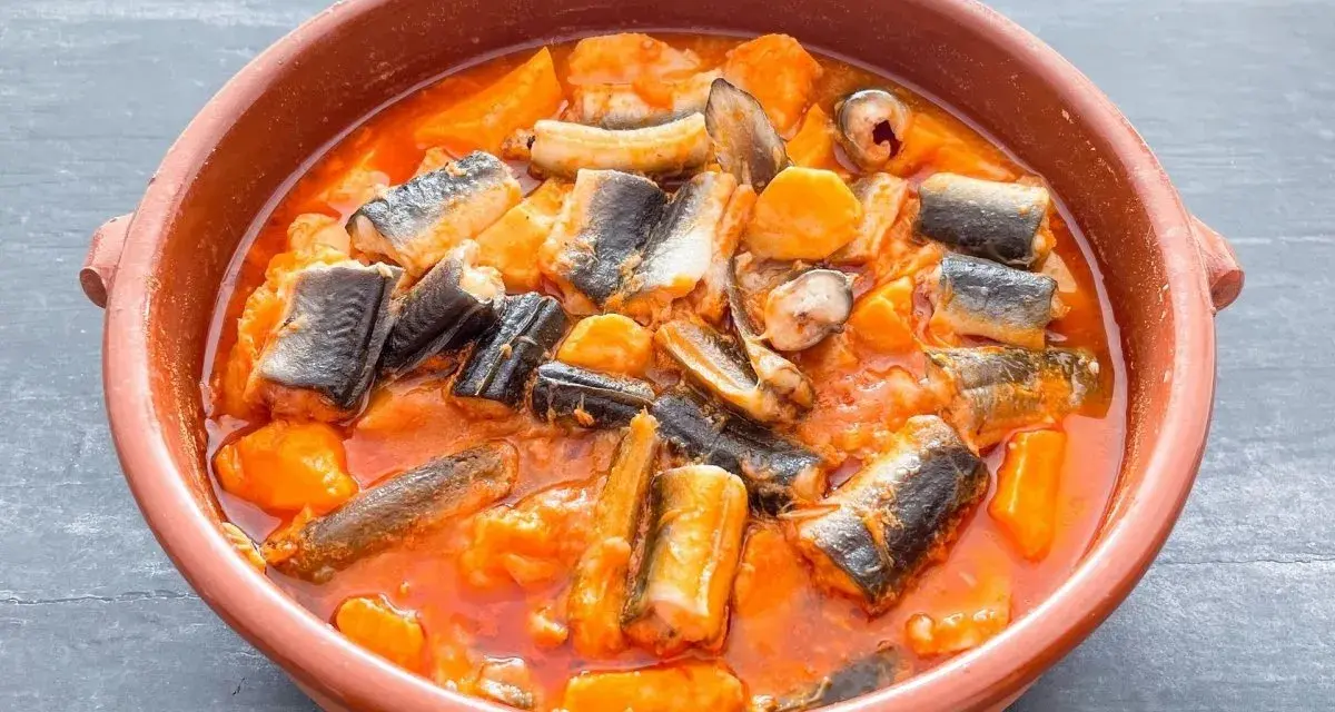 Un sabroso all i pebre en cazuela de barro, con trozos de anguila y patatas en una salsa rojiza.