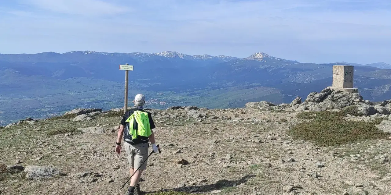 Senderista camina hacia el **puerto de Navafría**, con un mojón y montañas nevadas al fondo.