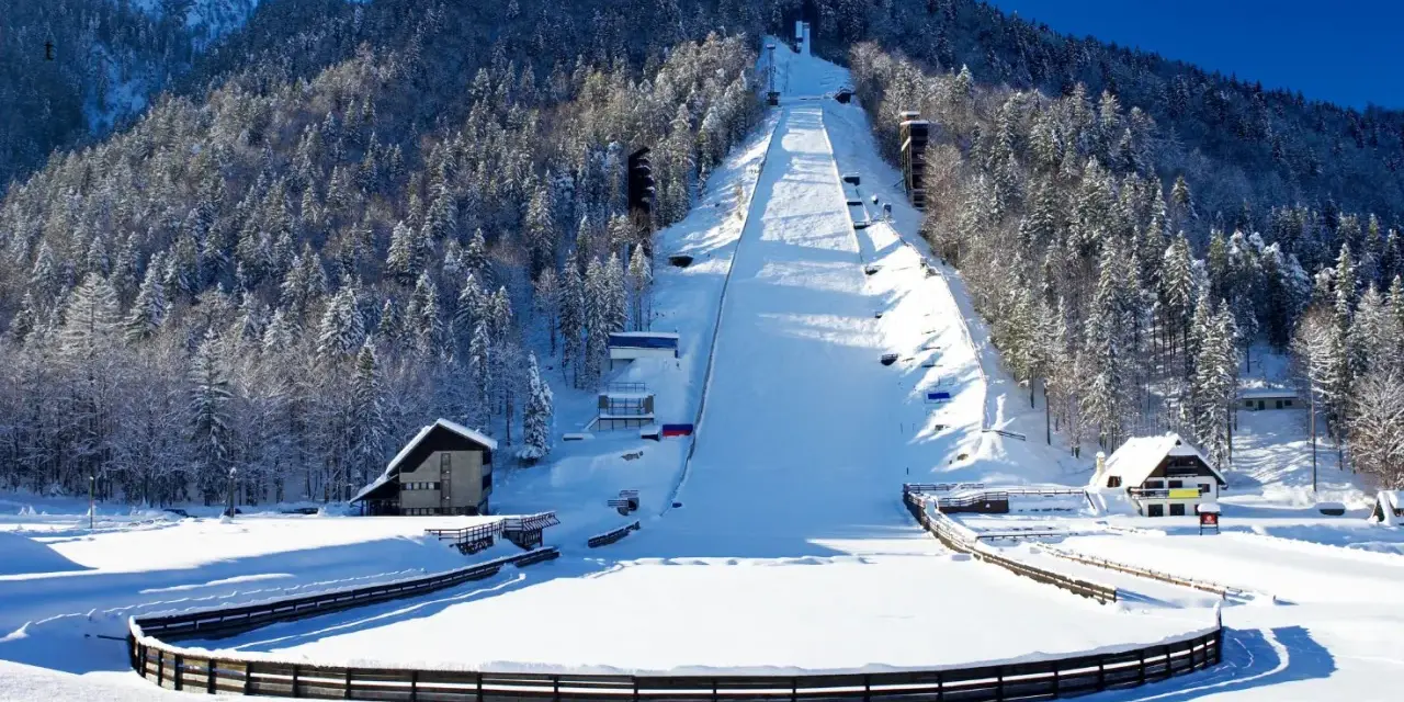 Zimowa Planica w Alpach Julijskich, z ośnieżoną skocznią narciarską i lasem iglastym.