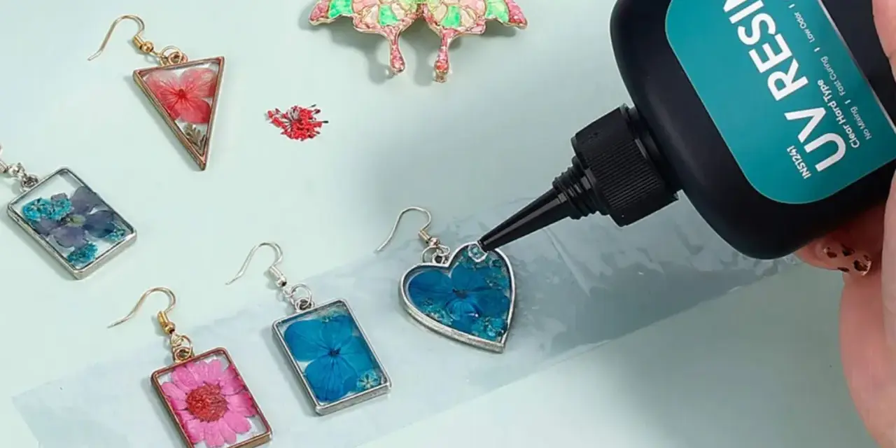 A hand applies UV resin to a heart-shaped earring with blue flowers, demonstrating how UV resin works to create beautiful jewelry.
