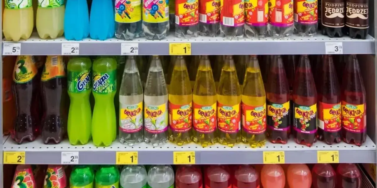 Półki sklepowe z różnymi napojami gazowanymi w plastikowych butelkach.
