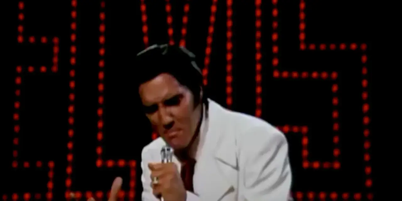Elvis Presley singt "If I Can Dream" in einem weißen Anzug vor einer roten Lichterwand.