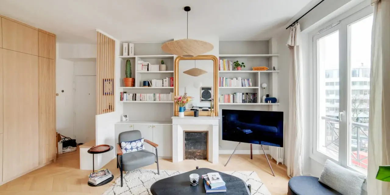 Aménagement entrée ouverte avec rangements boisés, fauteuil, cheminée décorative et étagères remplies de livres.