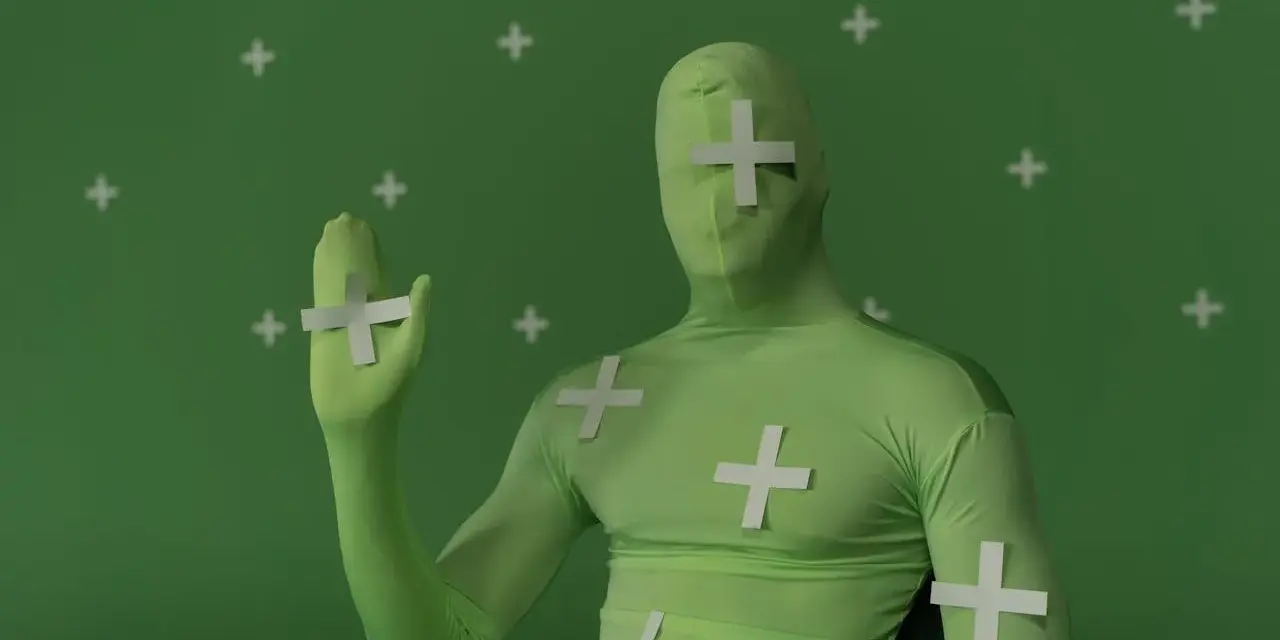 Persona in tuta verde con croci bianche, pronta per effetti speciali. Ecco come si usa il green screen per trasformare la realtà.