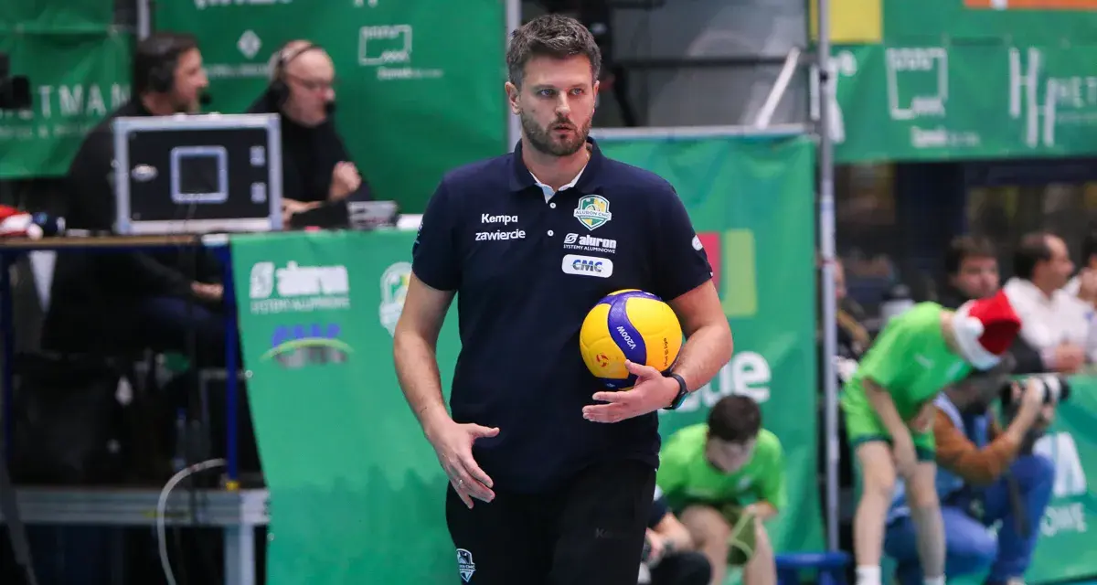 Trener Michał Piwowarczyk z piłką siatkową w dłoni, gotowy do akcji na boisku.