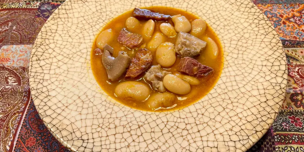 Plato de judiones de la granja receta tradicional, con trozos de tocino y carne en un caldo sabroso.