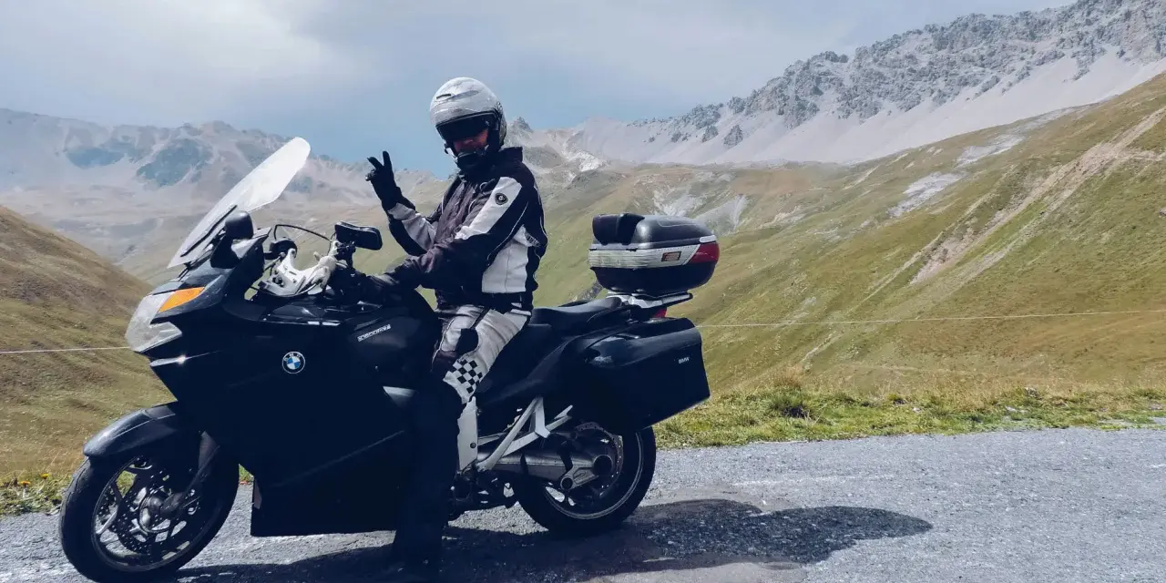 Motocyklista w kasku pozdrawia na tle gór. Przełęcz Stelvio zamknięta, ale widoki zapierają dech w piersiach.