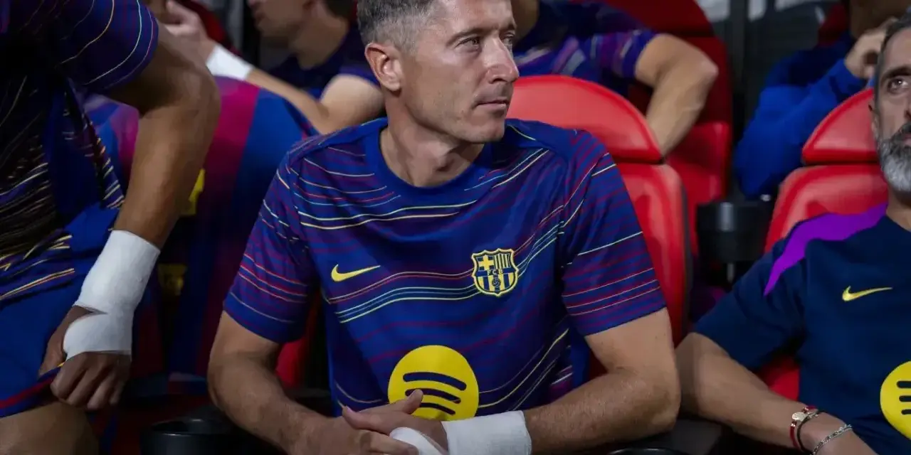 Robert Lewandowski w meczu FC Barcelona – Valencia CF, siedzi na ławce z bandażem na ręce, skupiony na grze.