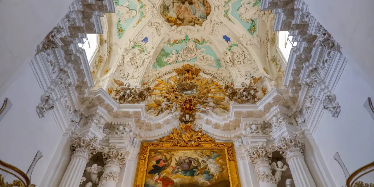 Magnifique plafond orné de fresques et de sculptures, typique du style baroque, avec un tableau doré au centre.