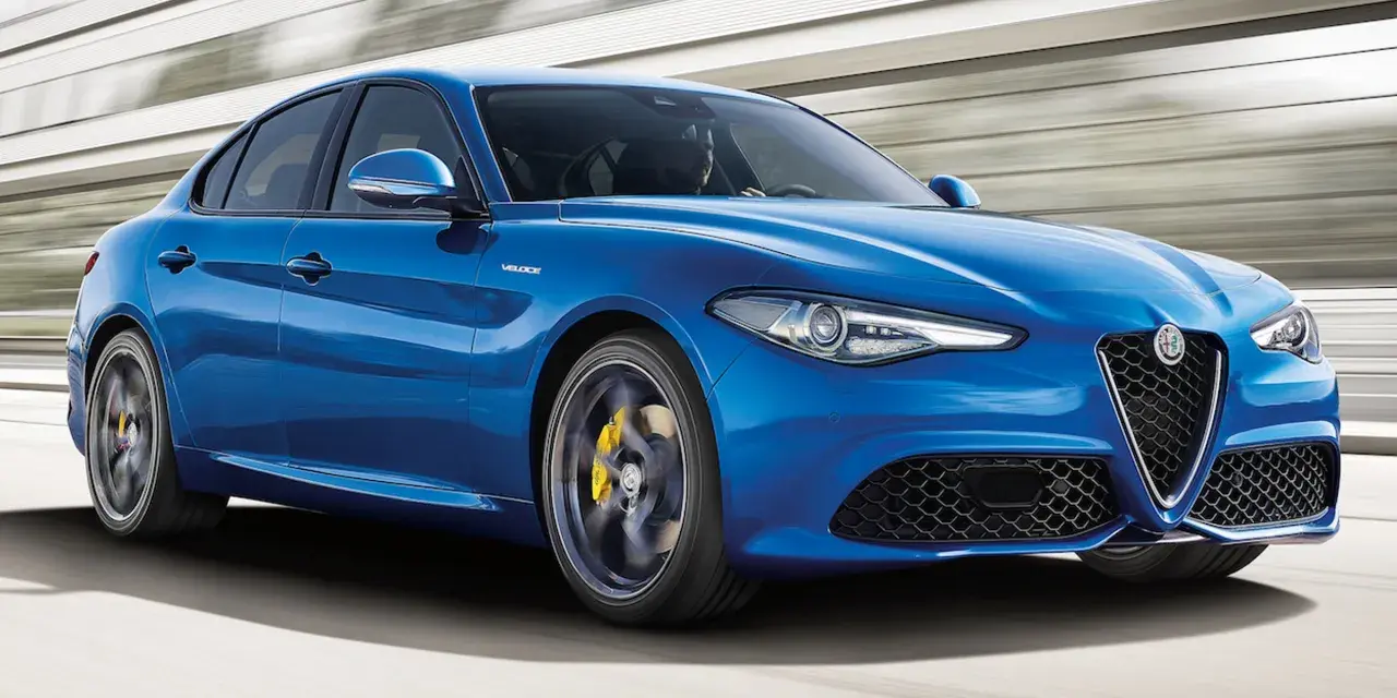 Błękitne Alfa Romeo Giulia Veloce pędzi po drodze, ukazując sportowy charakter i dynamiczną sylwetkę.