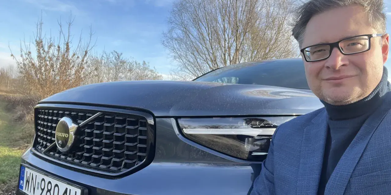 Mężczyzna w okularach i garniturze pozuje do zdjęcia z przodu Volvo XC40. Czy są jakieś wady tego modelu?