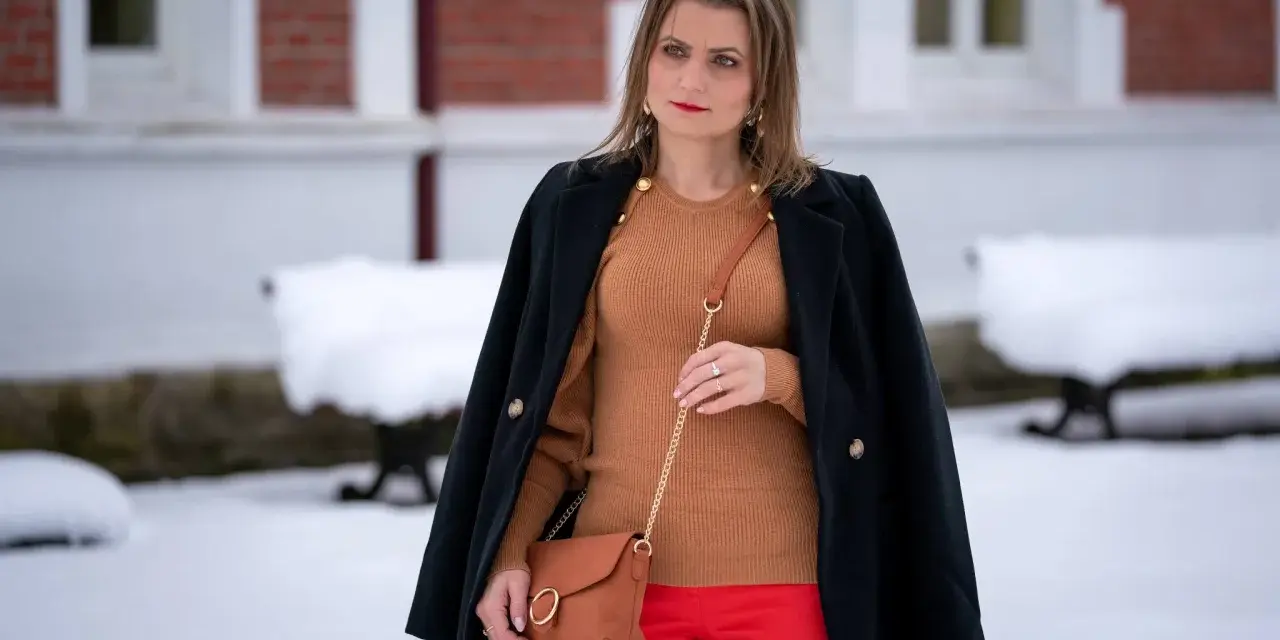 Elegancka stylizacja: co ubrać do czerwonej spódnicy? Brązowy sweter, czarny płaszcz i karmelowa torebka tworzą stylowy zestaw.