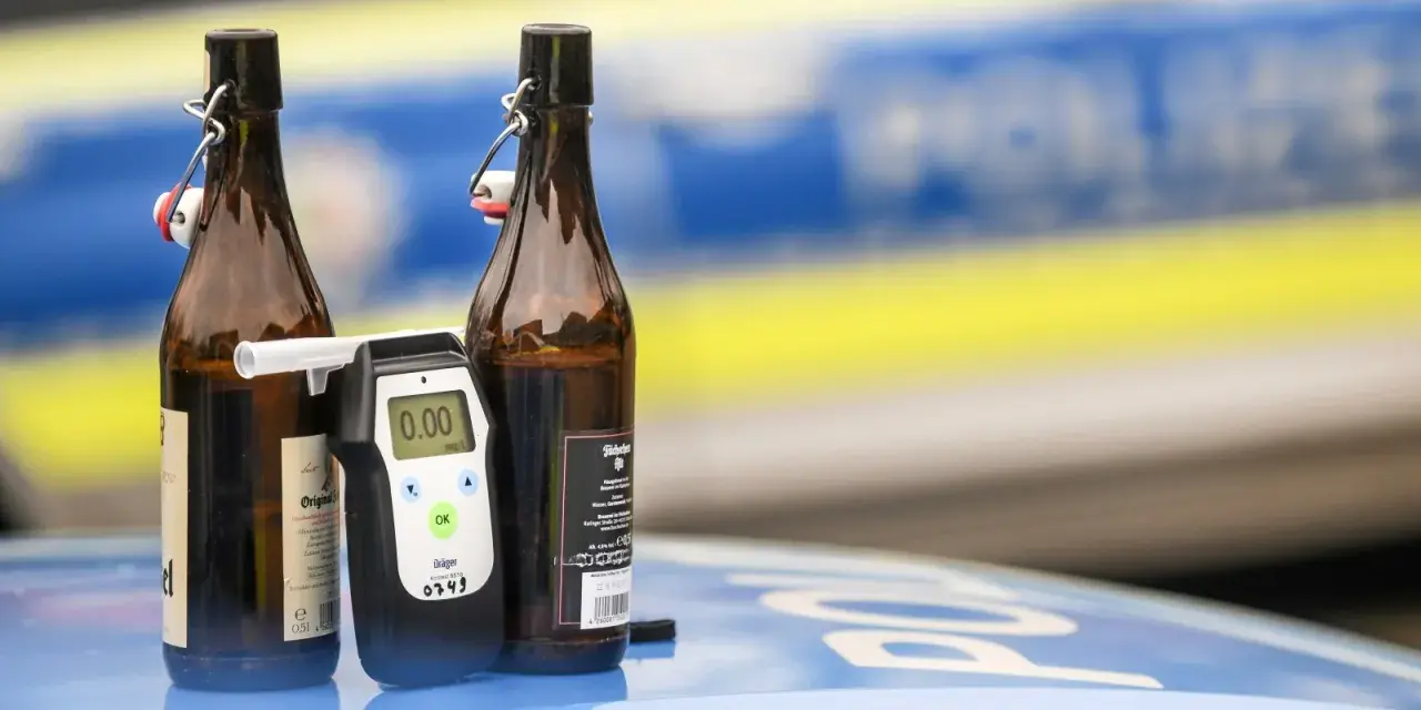 Zwei Bierflaschen und ein Alkoholtester auf einem Polizeiauto. Der Tester zeigt 0.00, aber die Gefahr einer 1 1 Promille Strafe bleibt.