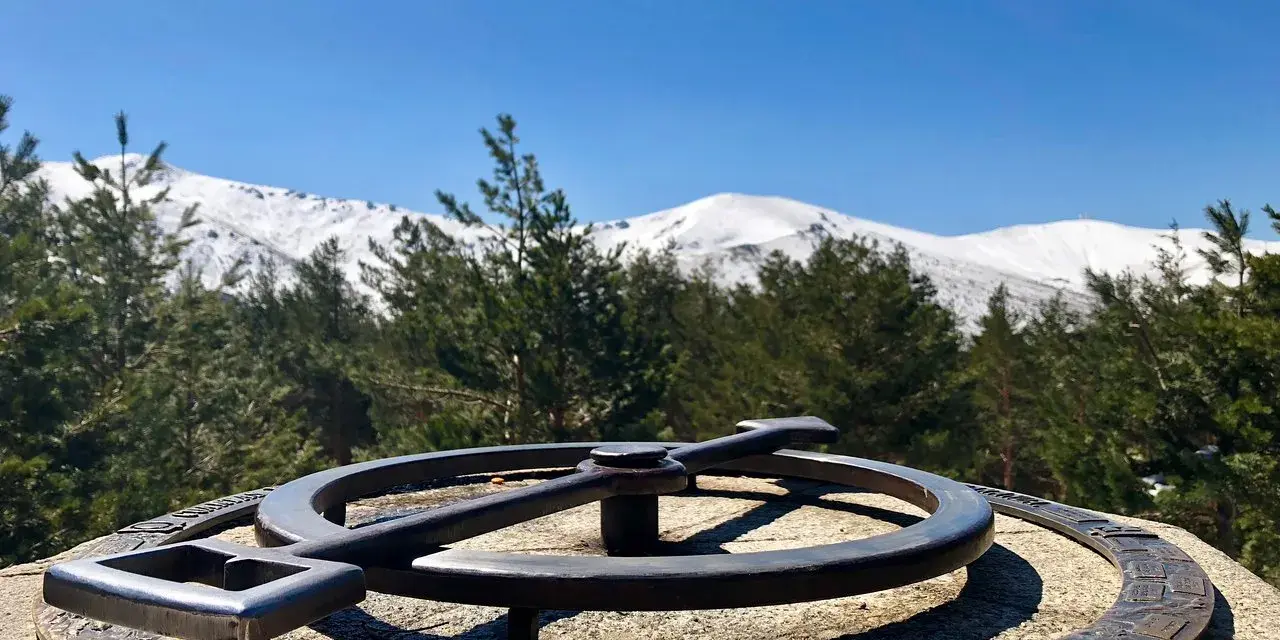 Un mirador de la gitana con un compás de bronce y montañas nevadas al fondo.