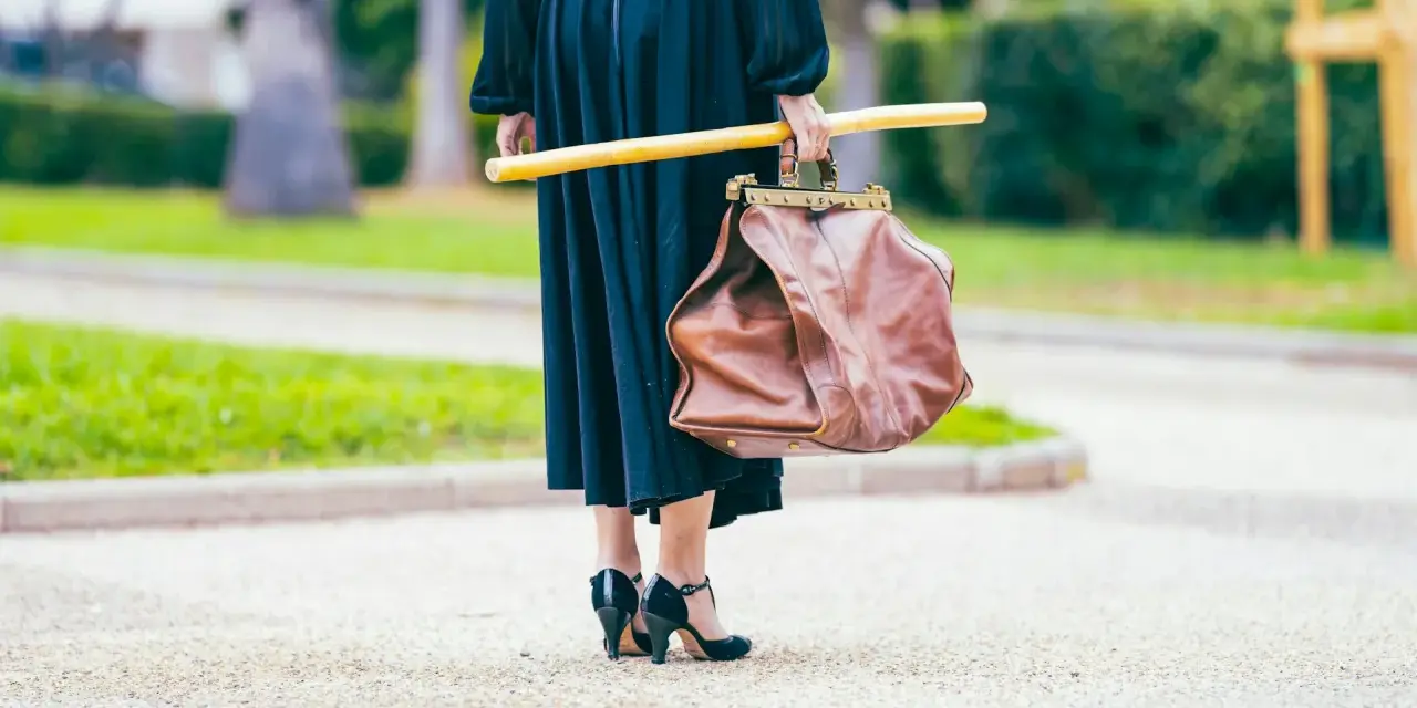Elegancka kobieta w czarnej sukni i czarnych szpilkach, niosąca brązową torbę i żółty kij. Uosobienie francuskiej mody.