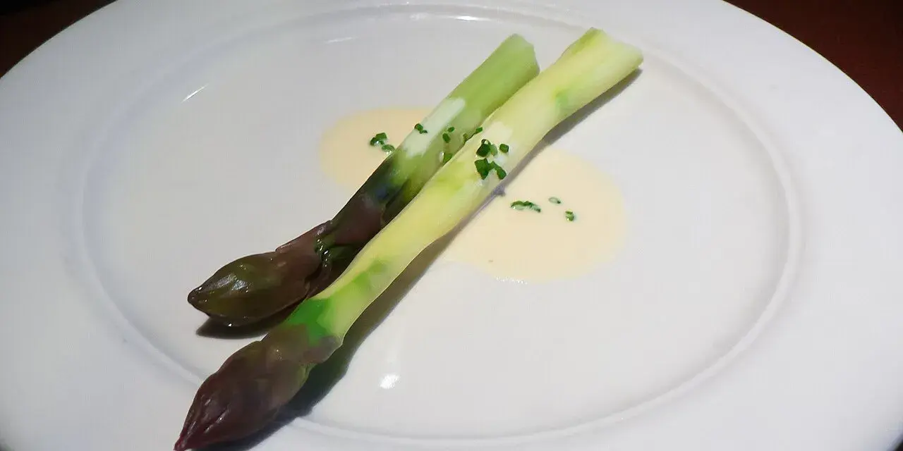 Zwei Spargelstangen auf einem Teller, serviert mit einer cremigen beurre blanc Sauce und gehackten Kräutern.