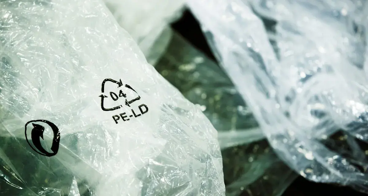 Zgniecione folie PE-LD z symbolem recyklingu. Firma stawia na recykling tworzyw sztucznych, dbając o środowisko.