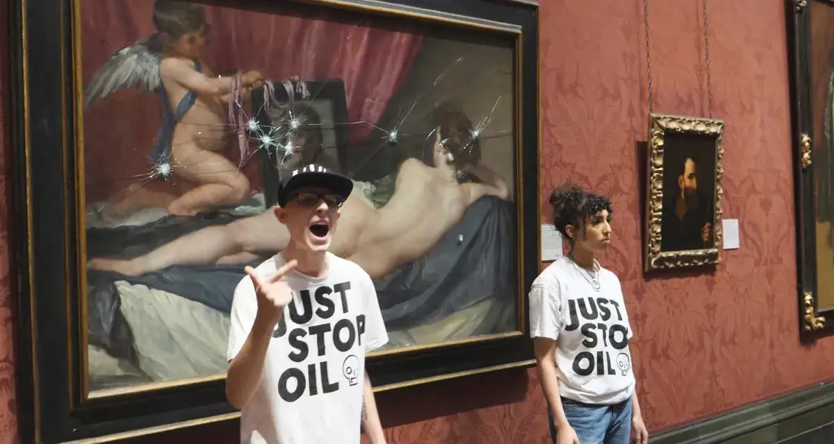Dwie osoby w koszulkach "Just Stop Oil" stoją przed obrazem "Wenus z lustrem", który został uszkodzony.