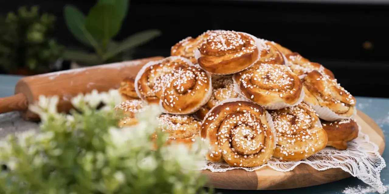 En hög med gyllene kanelbullar, redo att bakas enligt ett enkelt kanelbullar recept. En kavel ligger bredvid.