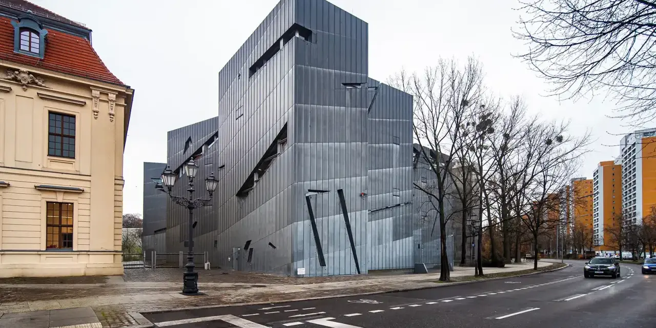 Nowoczesny budynek Muzeum Żydowskiego w Berlinie, obok zabytkowej kamienicy, z charakterystyczną, poszarpaną fasadą.