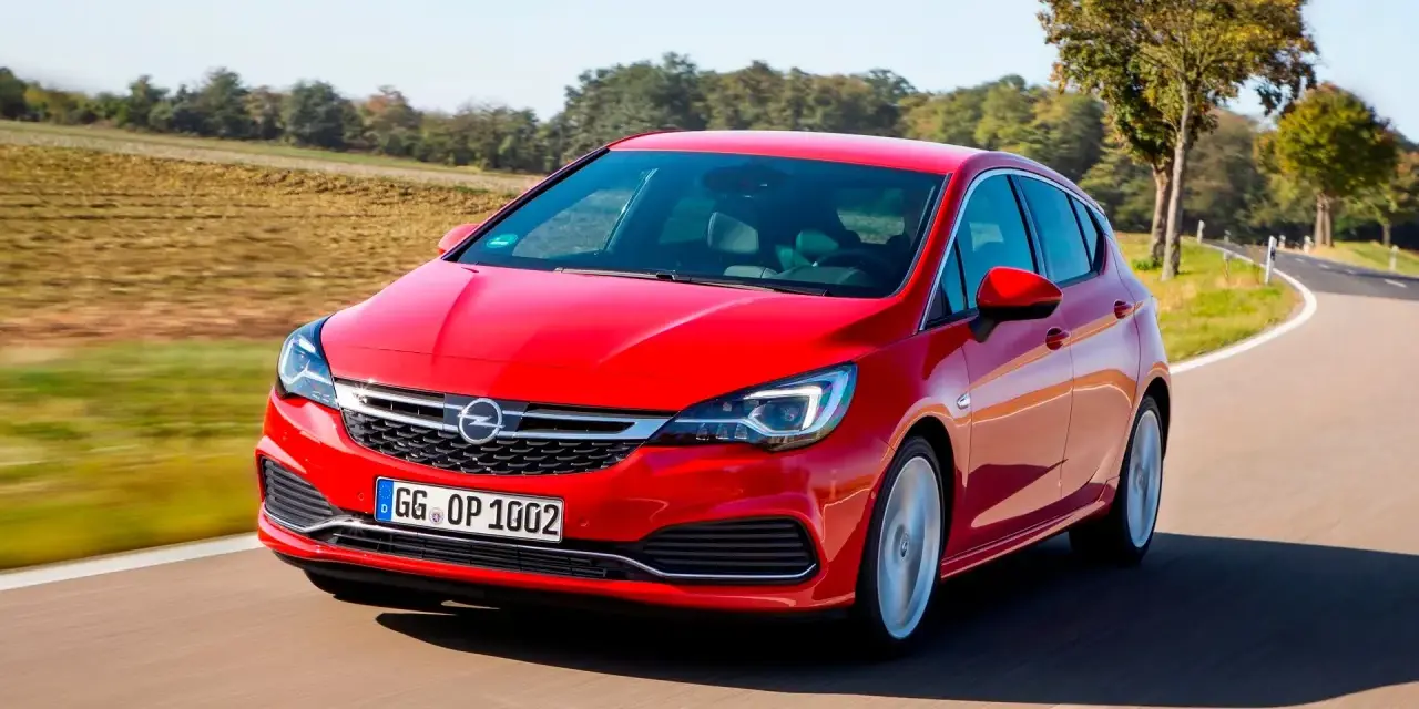Czerwony Opel Astra jedzie po krętej drodze. W tle pola i drzewa. Idealny do diagnostyki z **op-com opel po polsku**.
