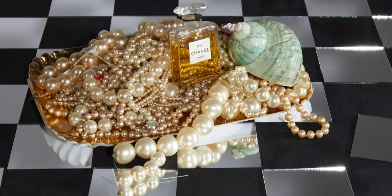 Perle, profumo Chanel N°5 e una conchiglia su un vassoio dorato. Il profumo evoca il **chanel significato** di lusso e raffinatezza.