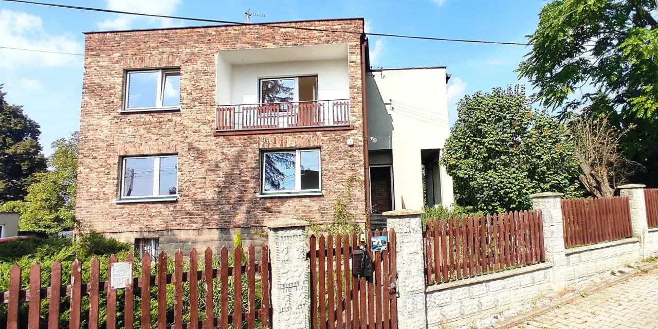 Nowoczesna metamorfoza domu z lat 80. z ceglaną fasadą, balkonem i drewnianym płotem.