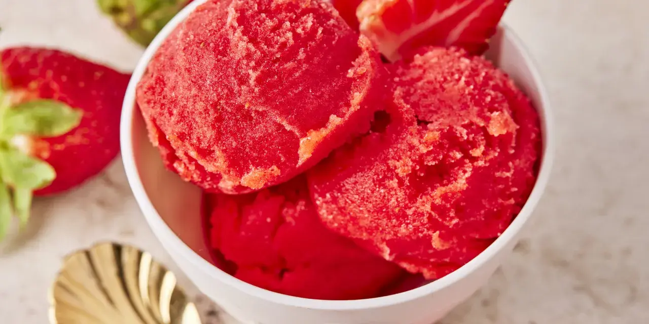 Schüssel mit erfrischendem Erdbeer Sorbet, garniert mit frischen Erdbeeren und einer goldenen Löffel.