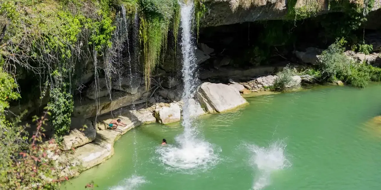 Disfrutando del baño en piscinas naturales junto a la cascada de Tobera. Un grupo de amigos se lanza al agua turquesa.