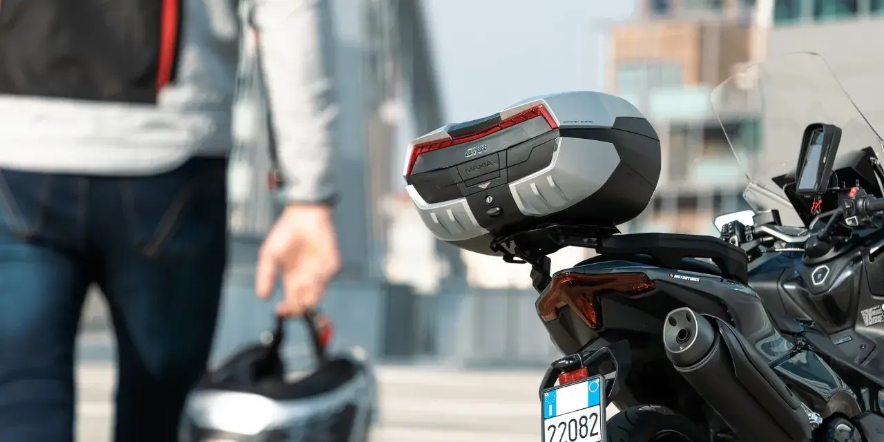 Un motociclista con casco in mano si avvicina alla sua moto. Andare in moto fa bene, un'avventura ti aspetta!