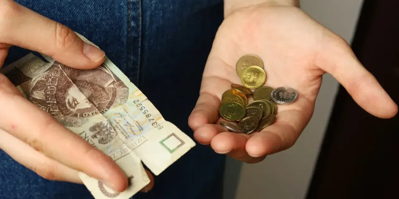 Dłoń trzyma banknot 20 zł i garść monet. Symbolizuje to spłatę długu po wyroku sądowym, gdzie każda złotówka ma znaczenie.