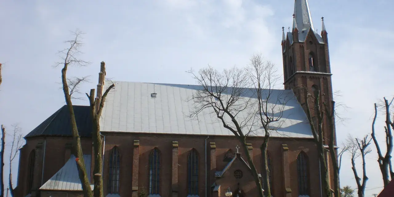Sanktuarium w Swarzewie, ceglany kościół z wysoką wieżą, otoczony drzewami o nagich gałęziach.