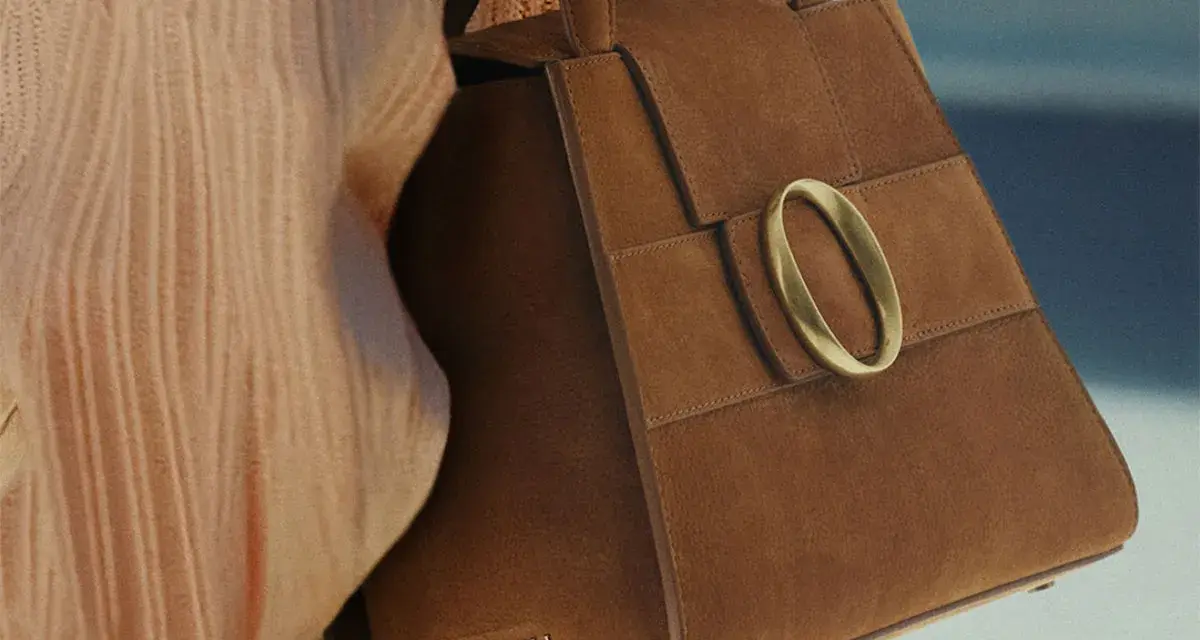 Borsa in camoscio marrone con fibbia dorata. La texture morbida evidenzia la differenza tra camoscio e pelle scamosciata.