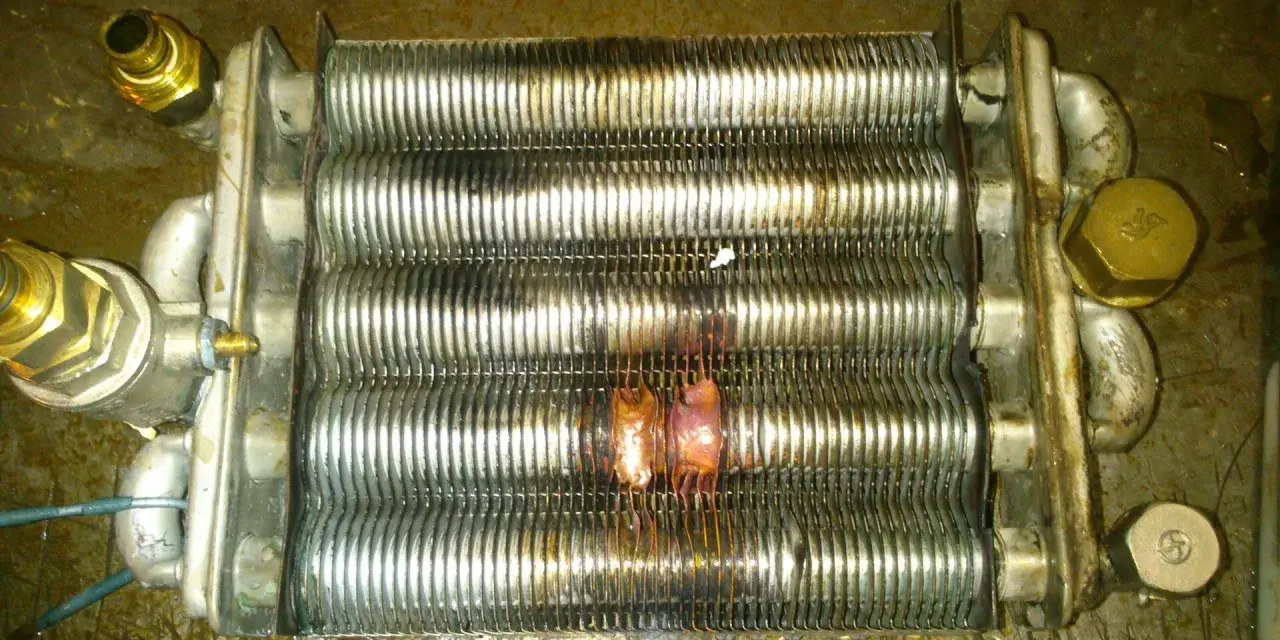 Scambiatore caldaia con evidenti segni di bruciatura, causa rottura scambiatore caldaia. Componenti metallici corrosi e deformati.