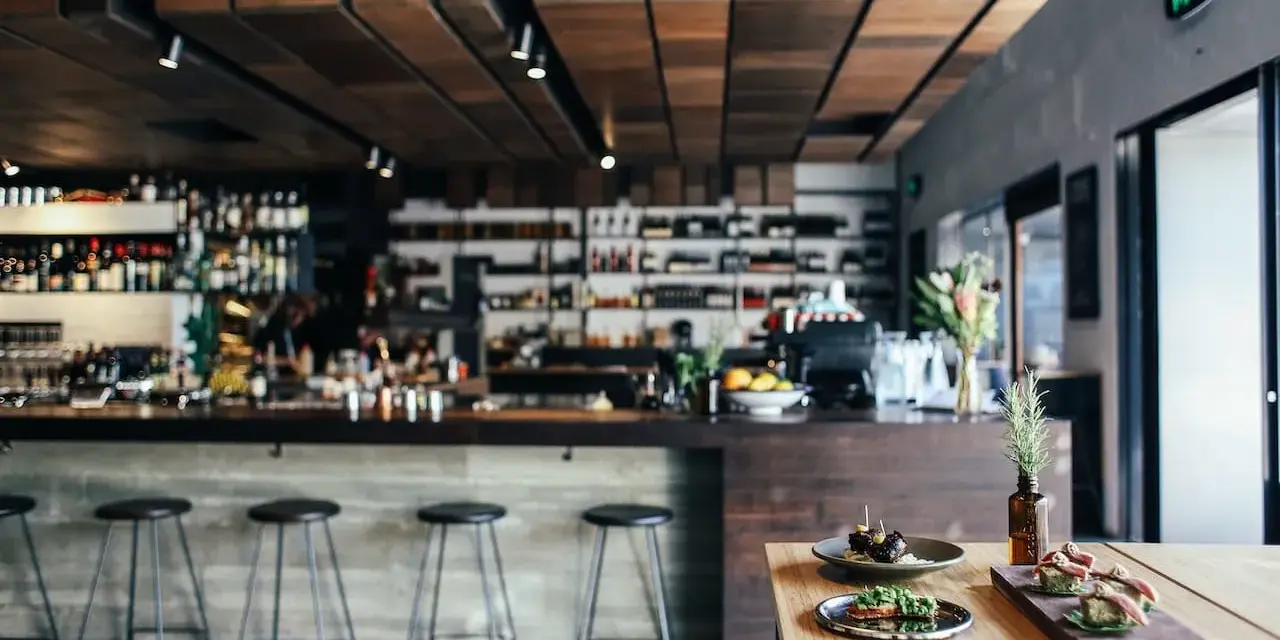 Ambiente restaurante moderno con barra, taburetes y aperitivos en mesa.