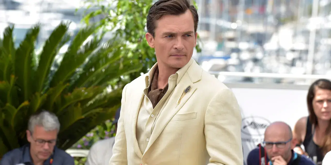Hombre con un impecable corte de pelo old money, viste un traje de lino color crema y un pañuelo de seda.