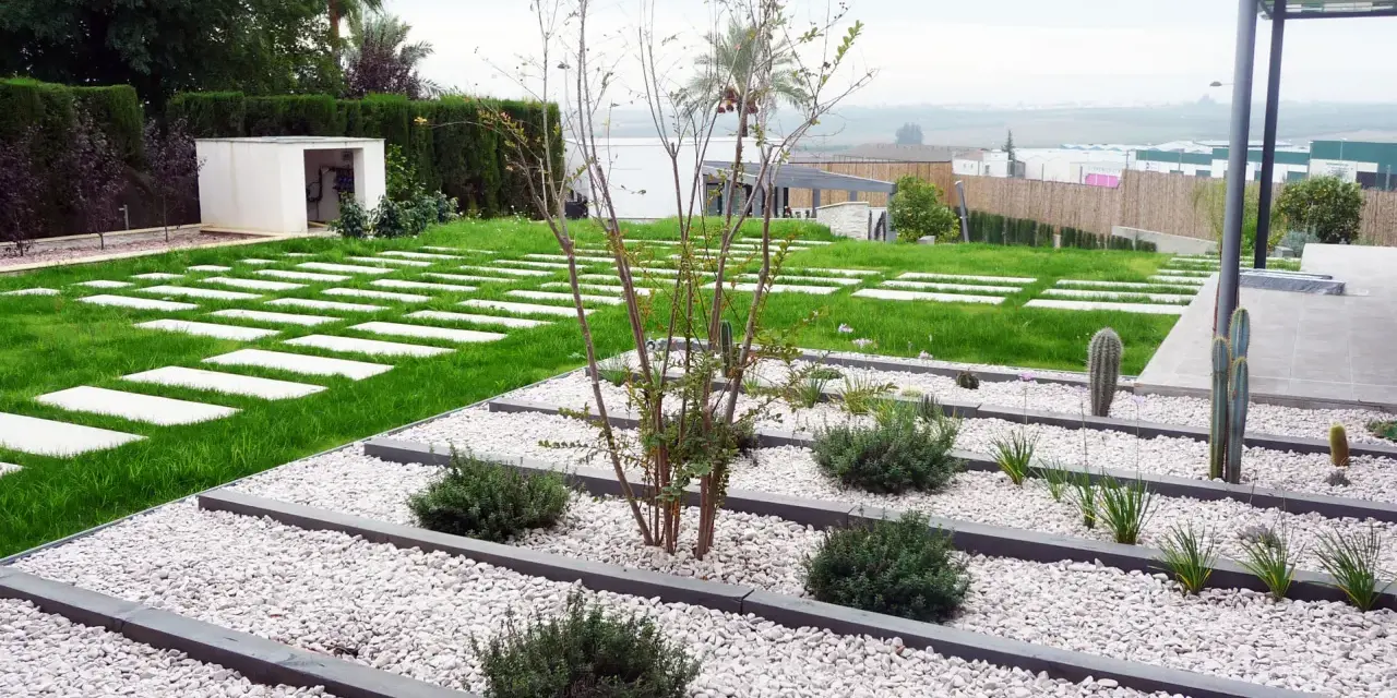 Vialetti giardino moderni con lastre quadrate su prato verde e aiuole di ghiaia bianca con piante succulente e arbusti.