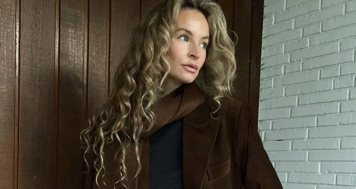 Kobieta z kręconymi, beżowymi włosami, którym pasuje ten odcień. Elegancka stylizacja z brązową marynarką.