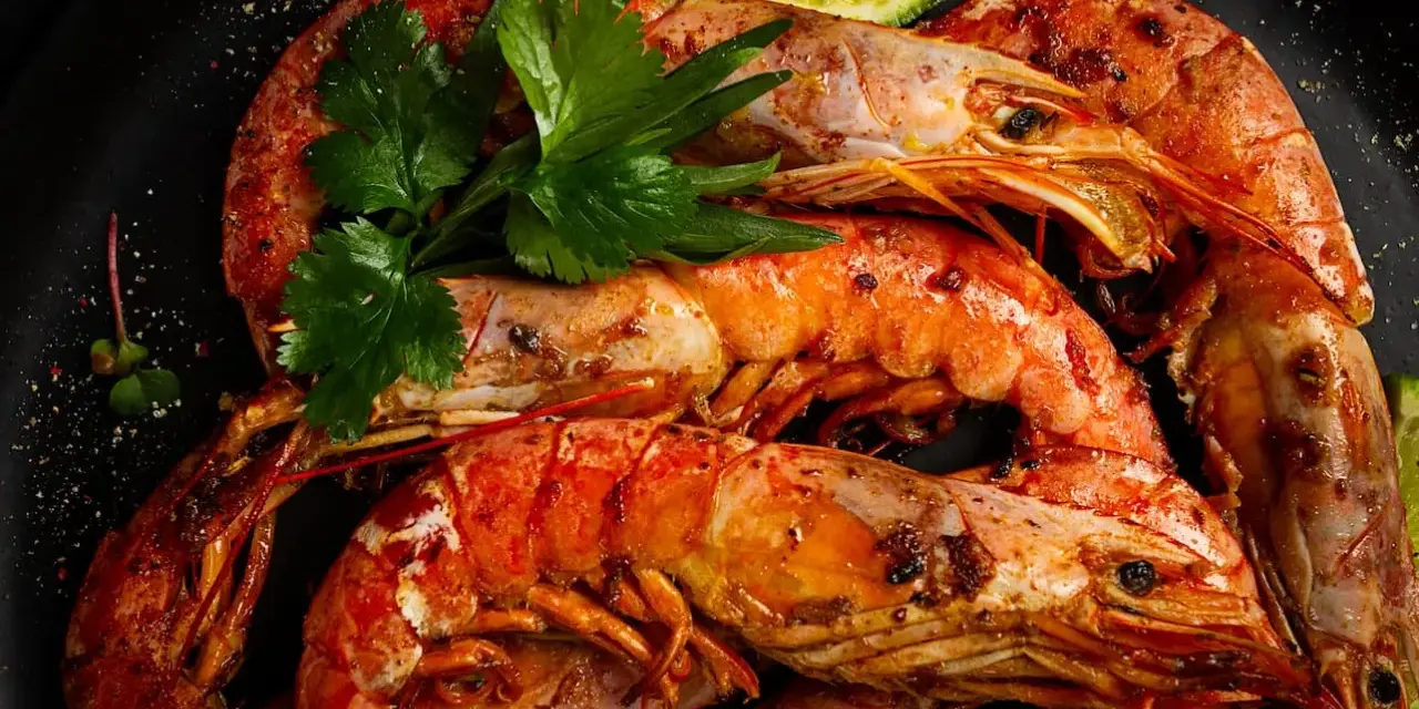 Gambones a la plancha, jugosos y dorados, servidos con perejil fresco y rodajas de lima. ¡Un manjar irresistible!