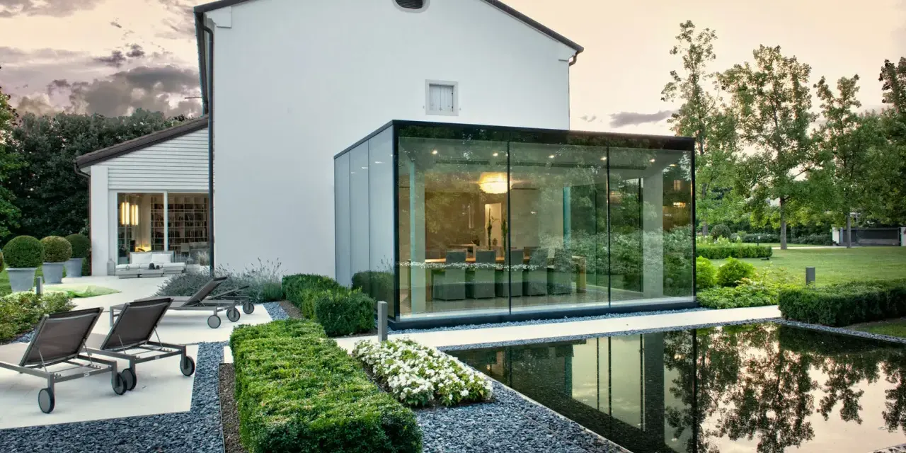 Ampliamento casa con estensione esterna in vetro, con piscina e arredi da giardino.