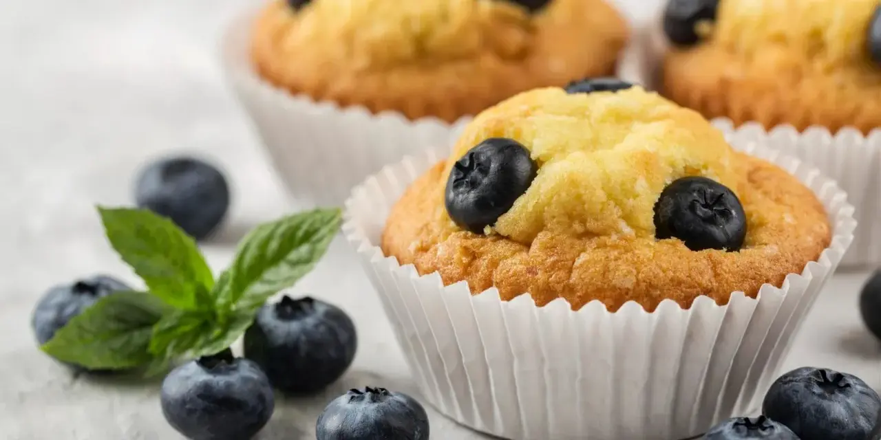 Pyszne muffiny z borówkami, ozdobione świeżymi owocami i listkiem mięty. Idealne na deser.