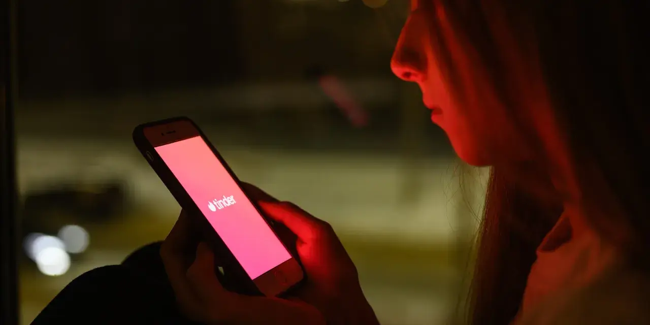 Dziewczyna patrzy na ekran telefonu z logo Tindera. Zastanawia się, co odpisać na "czego szukasz na Tinderze?".