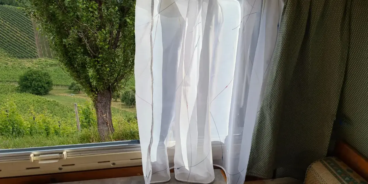 Leichte, transparente **Wohnwagen Gardinen Ideen** mit bunten Fäden vor einem Fenster mit Blick auf Weinberge.