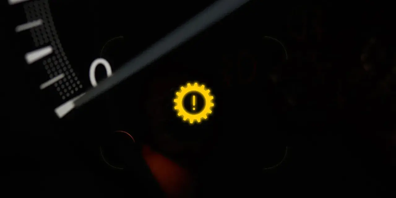 Gelbes Warnlicht mit einem Zahnrad und Ausrufezeichen im Auto-Armaturenbrett. Ein Zeichen für ein Problem mit dem Getriebe.